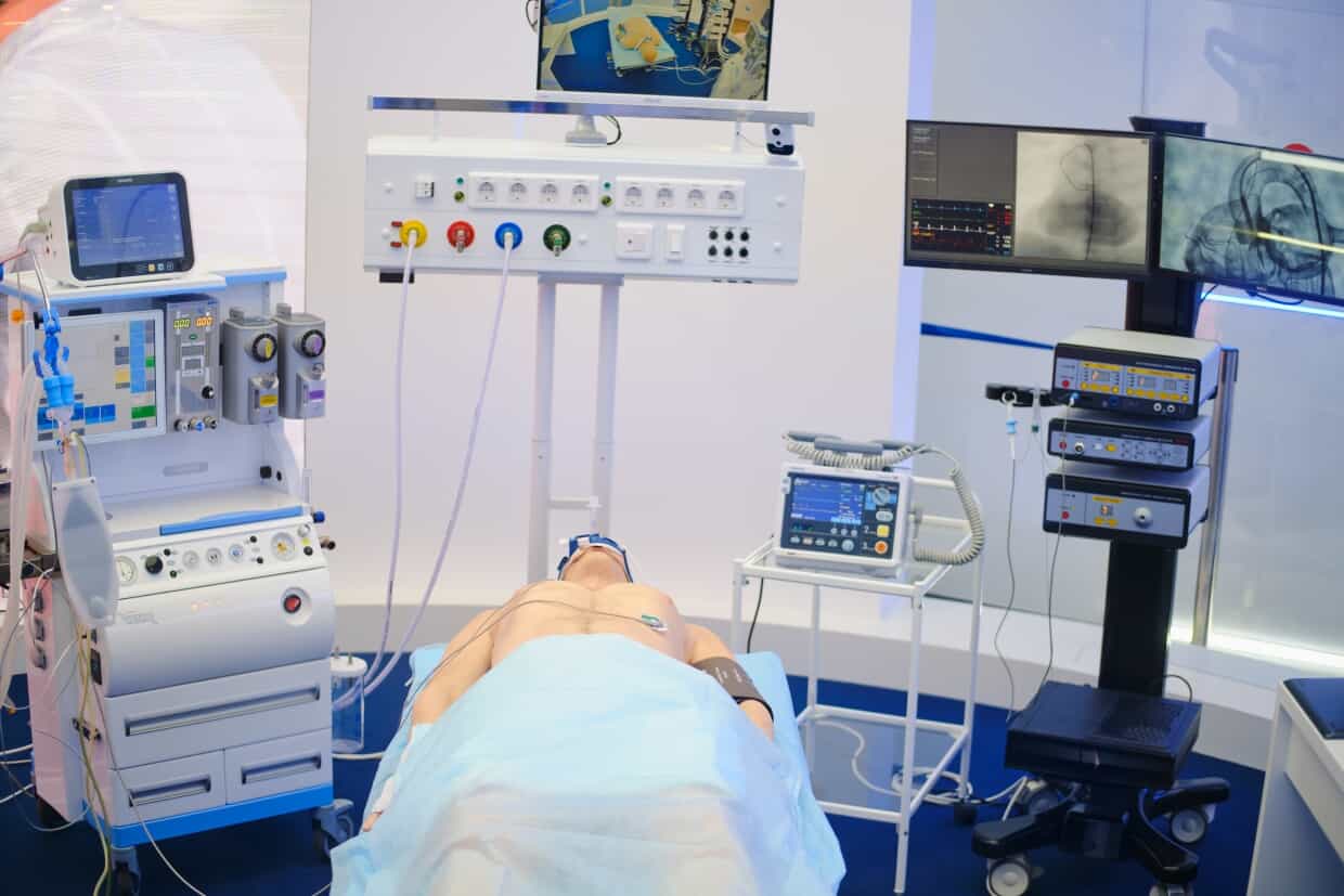 A person laying on a hospital gurney in a room full of medical machnes